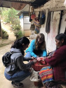 Two young women kneeling at a pot with a Guatemalan elder teaching them about the ceremony